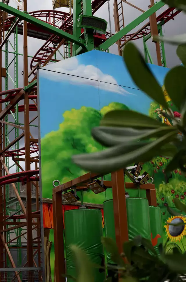 Das Foto zeigt eine Achterbahn mit einer grünen Rutsche in einem Vergnügungspark. Im Vordergrund sind der Himmel und einige Pflanzen zu sehen