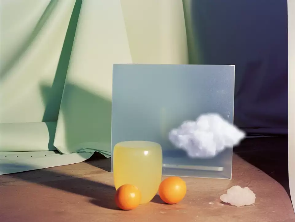 Das Bild zeigt eine Gruppe von Gegenständen auf einem Tisch in einem Innenraum, im Stil eines Stilllebens. Spiegel, Wolke Behälter 2 Ping-Pong Bälle..