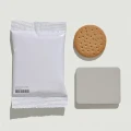 Drei Produkte der Marke IconScreen auf weißem Hintergrund angeordnet: eine weiße Verpackungstasche mit Barcode auf der linken Seite, ein rundes Keks mit Löchern oben rechts und ein graues rechteckiges Produkt darunter.