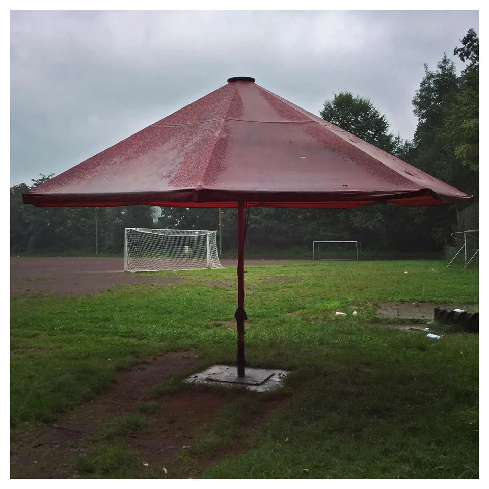 ein sehr gr0ßer Sonnenschirm im Regen auf einem Sportplatz