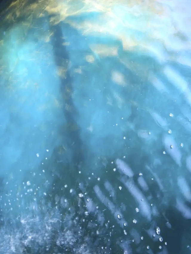 Abstrakte Unterwasserszene mit blauem Licht, das durch Wasser filtert, und glitzernden Partikeln, die in der Strömung treiben. Die verschwommene Komposition erzeugt eine ruhige, meditative Atmosphäre.