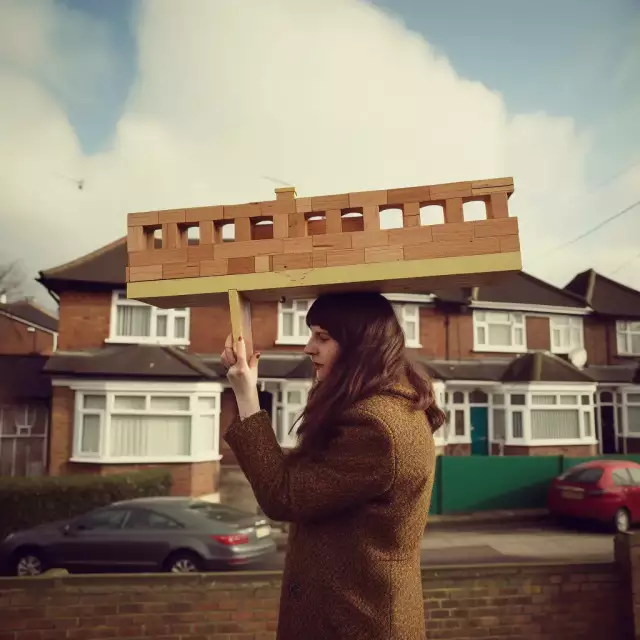 KI-generiertes Foto aus dem England der 1970er Jahre: Eine 30-jährige Architekturstudentin präsentiert ihr hölzernes Architekturmodell.