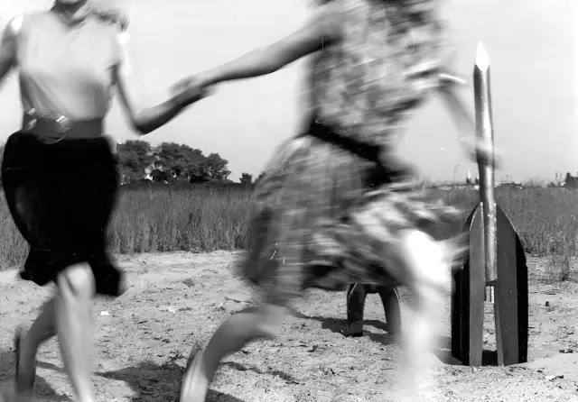 Zwei junge Frauen - Raketenmädchen - entfernen sich von 2 startenden Holzraketen. Die schwarz-weiße Aufnahme zeigt sie in einer dynamischen Pose.