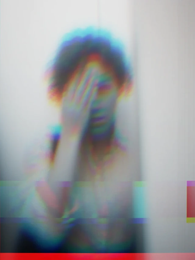 Eine unscharfe, verzerrte Aufnahme einer Person, die ihr Gesicht mit der Hand verdeckt, mit Chromatic-Aberration-Effekten in Blau, Rot und Grün. Die Darstellung wirkt experimentell und digital verfremdet.