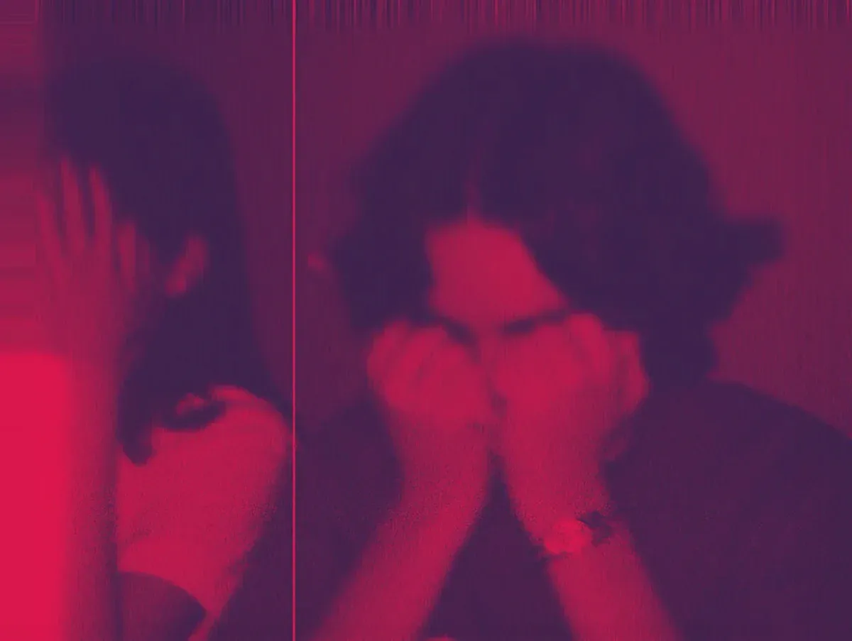 Eine Person sitzt vor einem Spiegel in rotem Neonlicht und betrachtet ihr Spiegelbild. Das Bild zeigt eine symmetrische Komposition mit gespiegelten Silhouetten vor intensiv leuchtendem magenta-rosa Hintergrund.