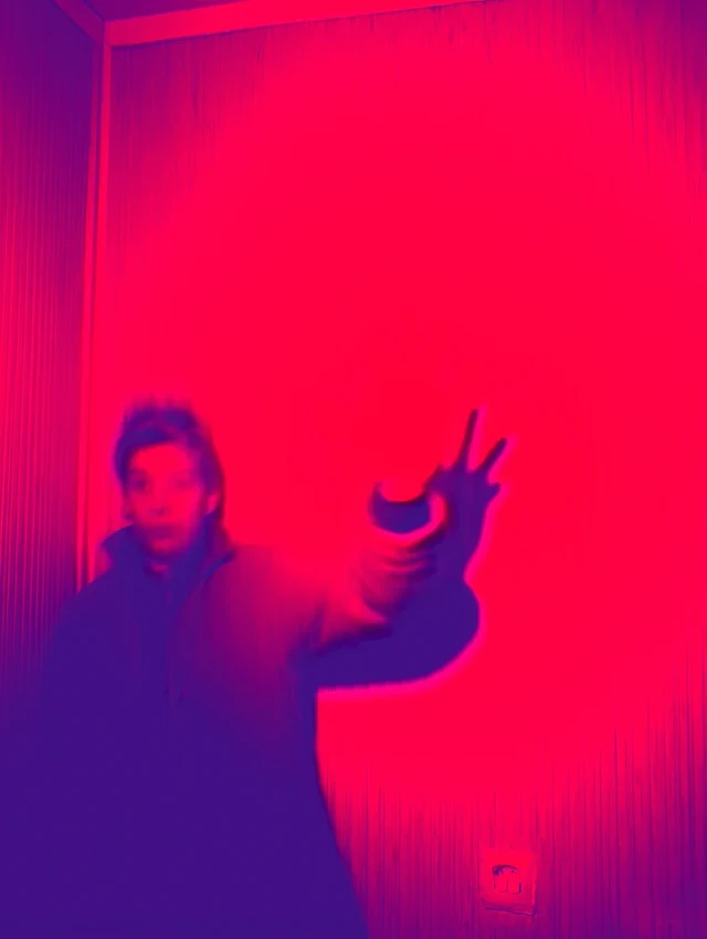 Eine Person steht vor einer leuchtend rosa-roten Wand und hält ihre Hand in einer ausdrucksstarken Geste nach oben. Das Bild hat eine intensive neon-ähnliche Beleuchtung mit Blau- und Rottönen, die eine futuristische Atmosphäre schafft.