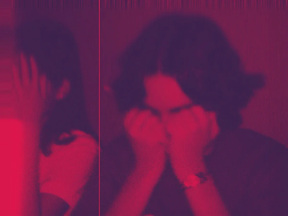 Eine Person sitzt vor einem Spiegel in rotem Neonlicht und betrachtet ihr Spiegelbild. Das Bild zeigt eine symmetrische Komposition mit gespiegelten Silhouetten vor intensiv leuchtendem magenta-rosa Hintergrund.