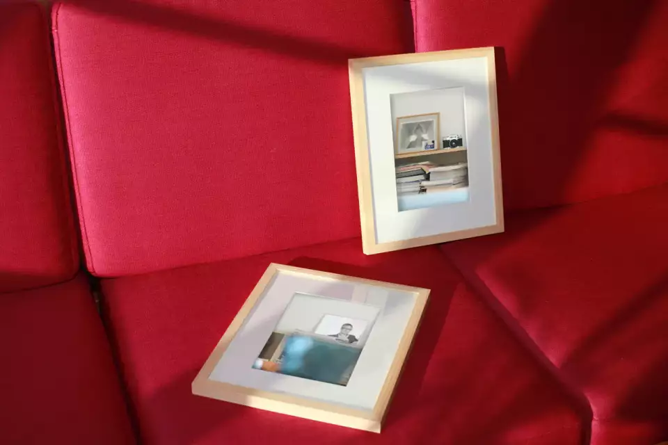 Das Bild zeigt 2 Bilderrahmen mit Fotografien, die auf einer roten Couch liegen. In den Bilderrahmen sind alte Bürofotografien von IconScreen abgebildet.