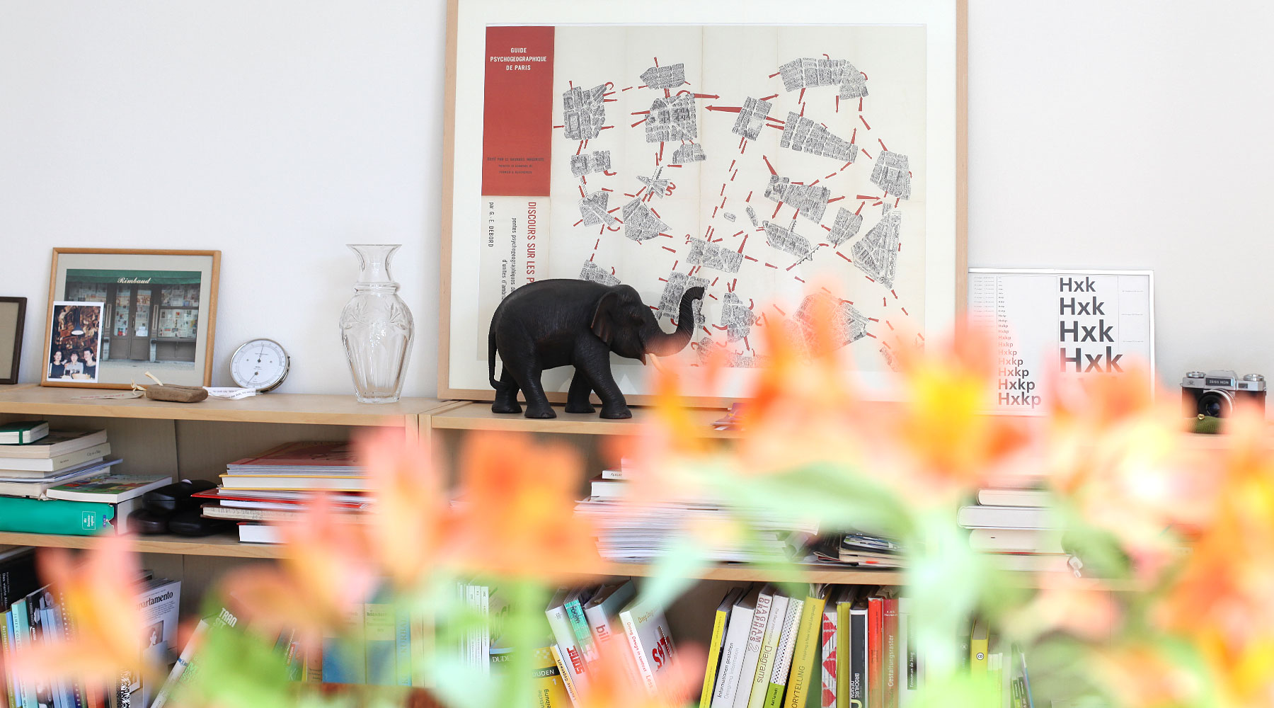 Innenansicht Agentur, Bücherregal mit einer Karte der Situationisten: Psychogeographic guide of Paris, sowie Vase, Hydrometer und Bilderrahmen.