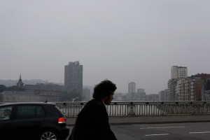ein trauriger nebeliger Tag in Lüttich, ein fahrradfahrer im Profil quert eine Brücke über die Maas